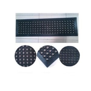 Rectangular black rubber mat with evenly spaced circular holes on a tiled floor while viewed from above.