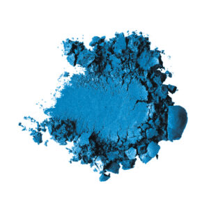 Blue pigment powder scattered in a loose pile on a white background, with darker chunks at the edges