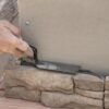 Close-up of a hand spreading gray mortar with a trowel onto a stacked stone wall surface.