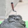 Trowel embedded in a mound of wet concrete on a bright green work surface outdoors.