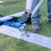 Person in gloves tightening a metal frame clamp on grass during outdoor assembly work.