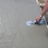 Worker smooths a freshly poured concrete slab with a hand trowel along the edge of formwork
