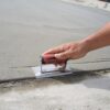 Hand using a red Marshalltown concrete trowel to smooth a freshly poured slab edge