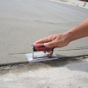 Hand using a red Marshalltown concrete trowel to smooth a freshly poured slab edge