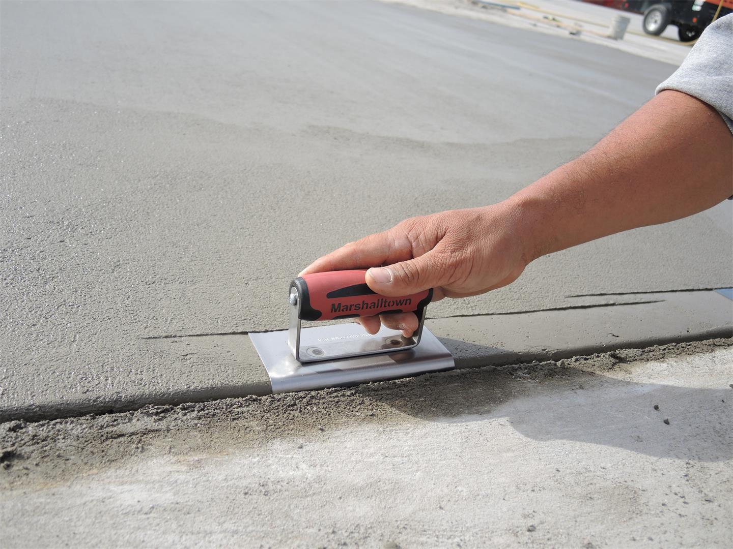 Hand using a red Marshalltown concrete trowel to smooth a freshly poured slab edge